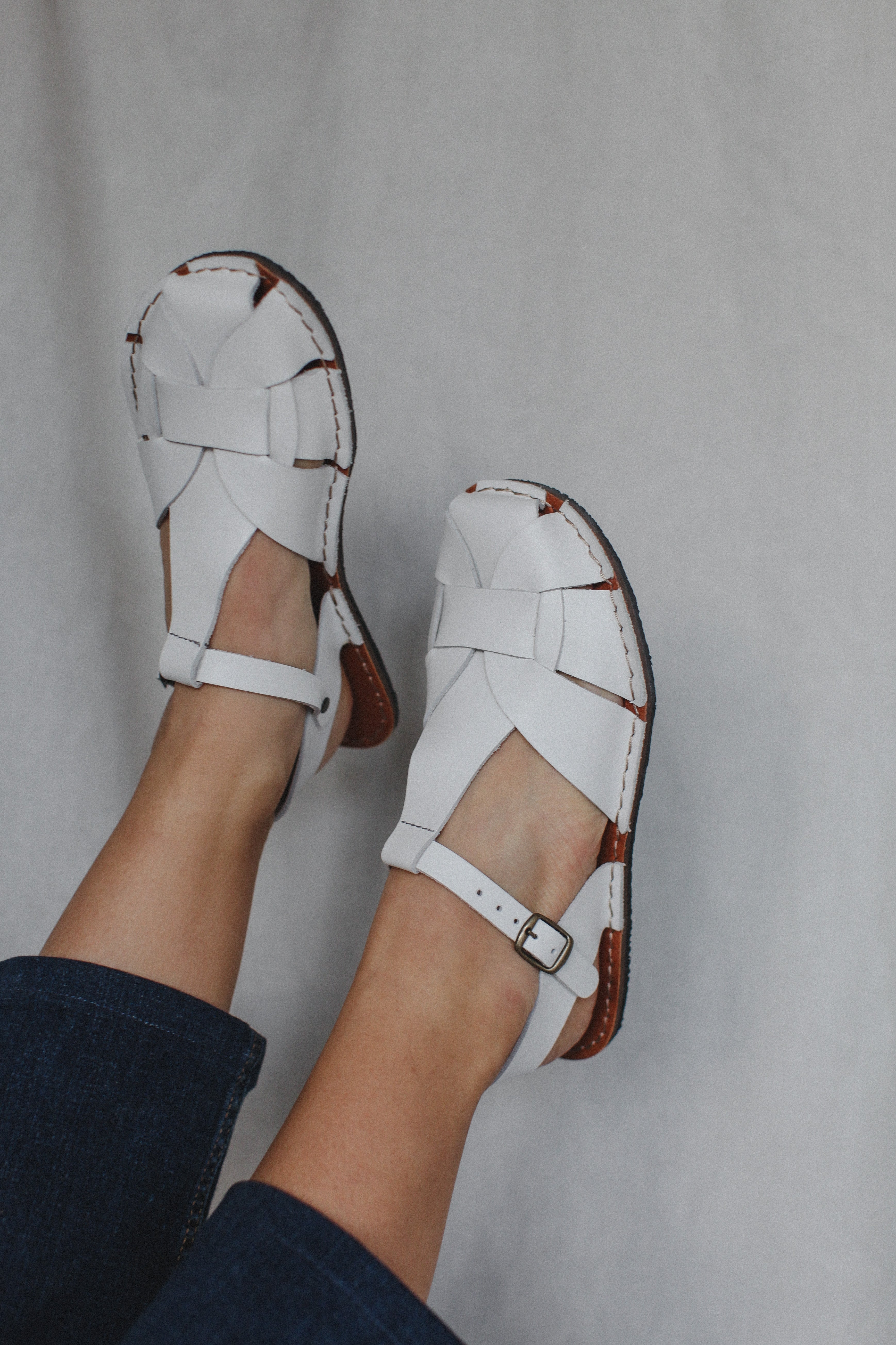 White sandals with brown accents worn by a person on a gray background
