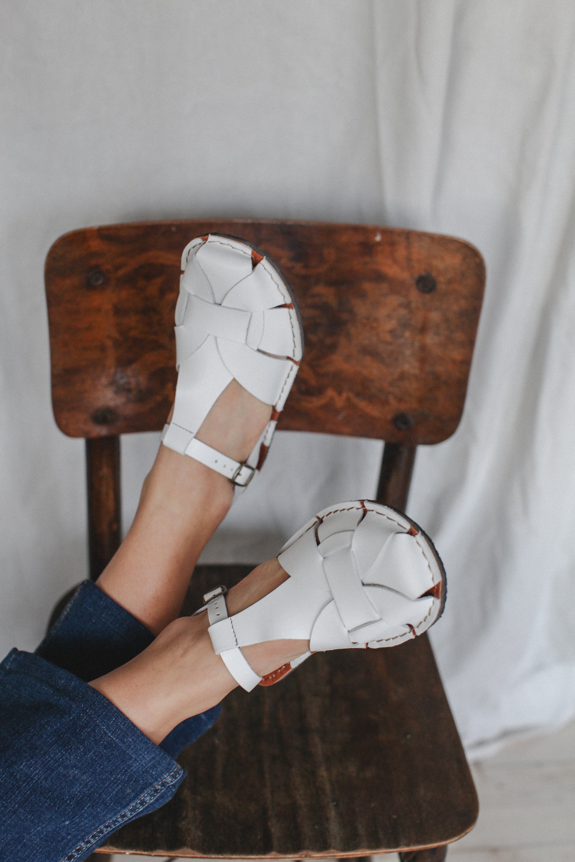 White barefoot sandals being worn on a wooden chair with a neutral background