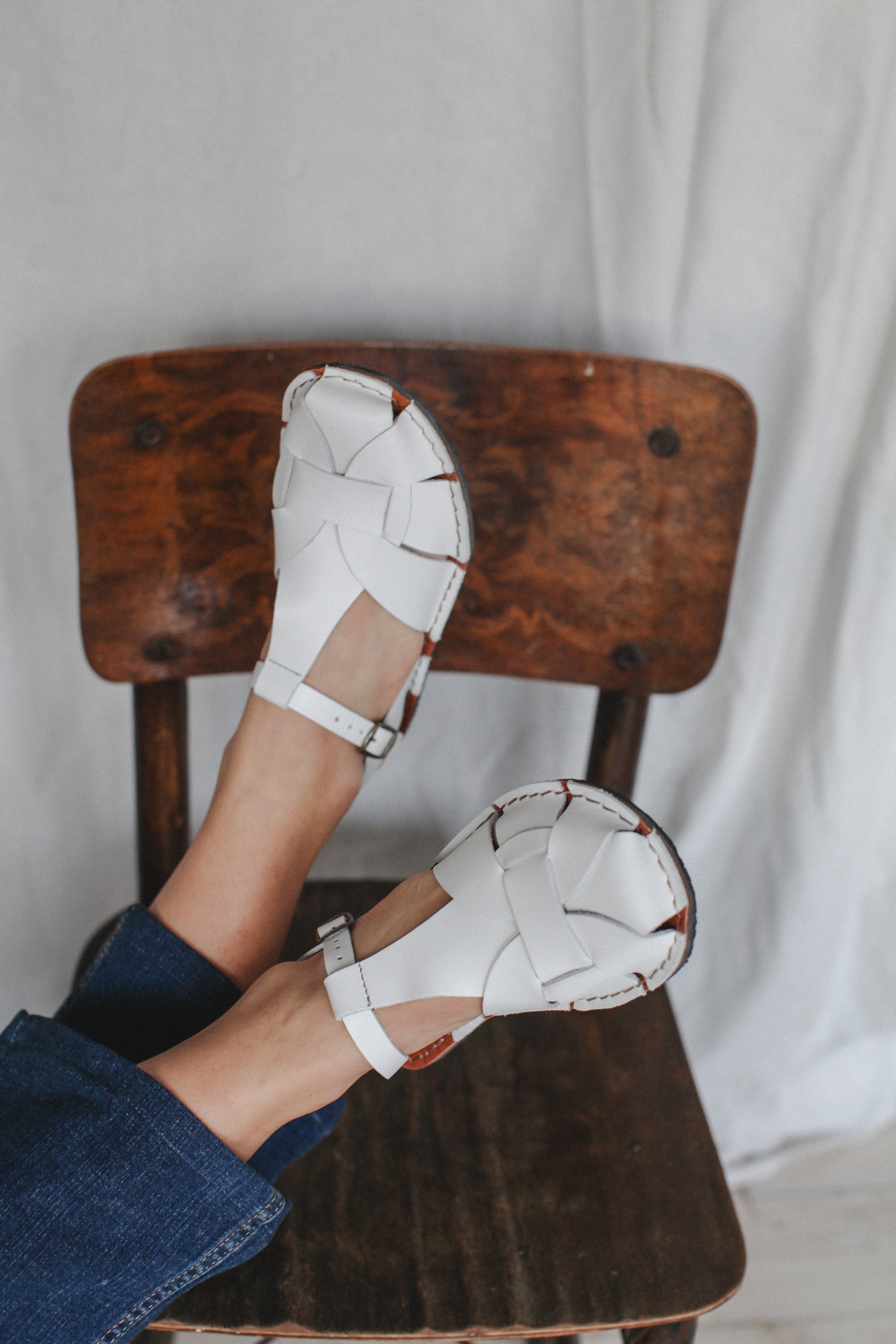 White barefoot sandals being worn on a wooden chair with a neutral background